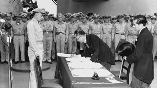 Japanese Foreign Minister Mamoru Shigemitsu signs the Instrument of Surrender on behalf of the Japanese Government, on board USS Missouri (BB-63), 2 September 1945. Lieutentant General Richard K. Sutherland, U.S. Army, watches from the opposite side of the table. Foreign Ministry representative Toshikazu Kase is assisting Mr. Shigemitsu. Photograph from the Army Signal Corps Collection in the U.S. National Archives.